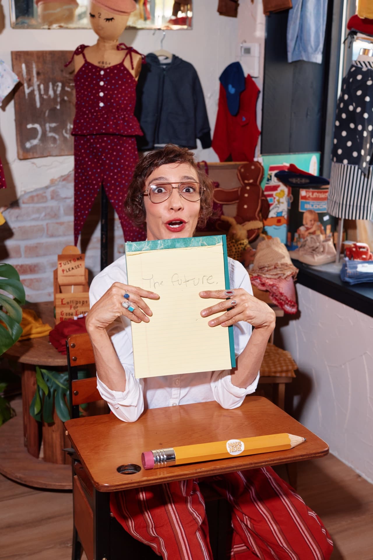 Priscilla Barroso at a school desk in her studio, holding up a yellow legal pad that reads The future.