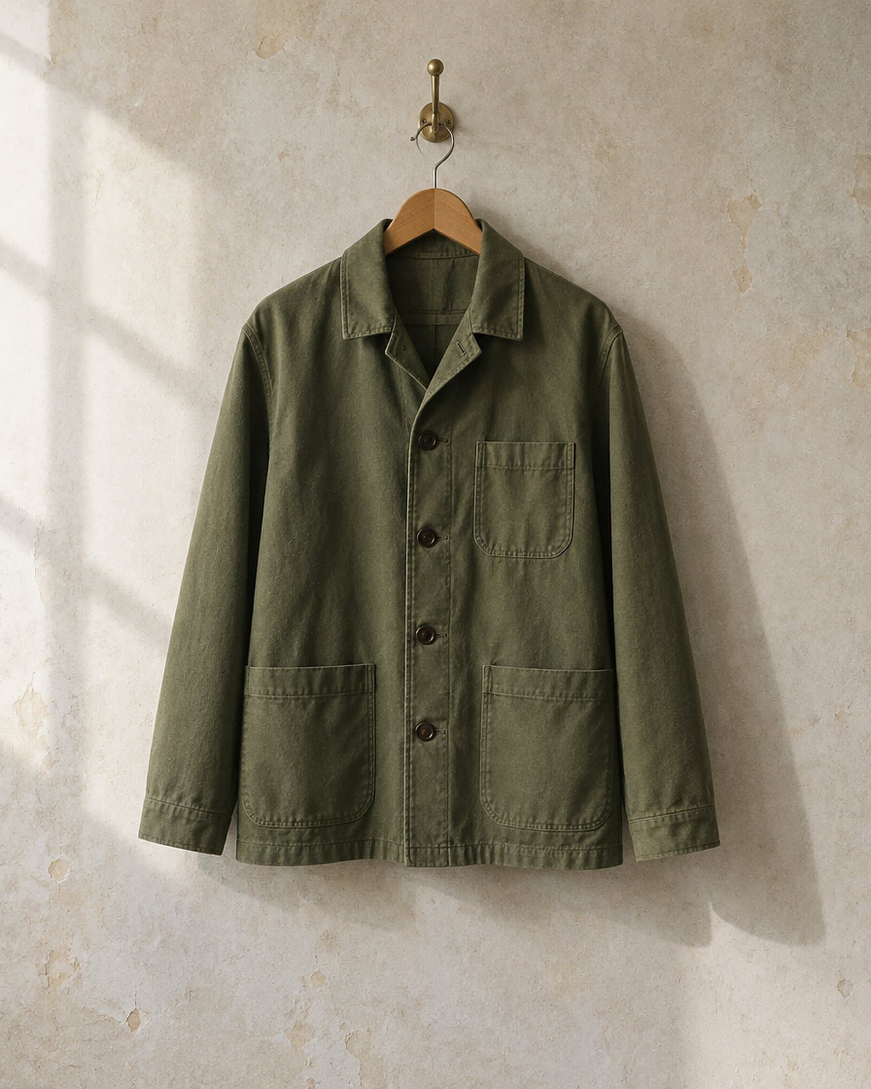 A finished olive chore jacket hanging on a brass hook.